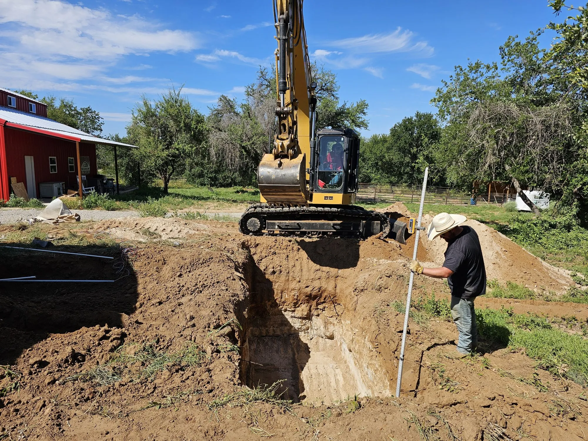 A Ledford Services excavator digging the tank hole while a technician checks grade