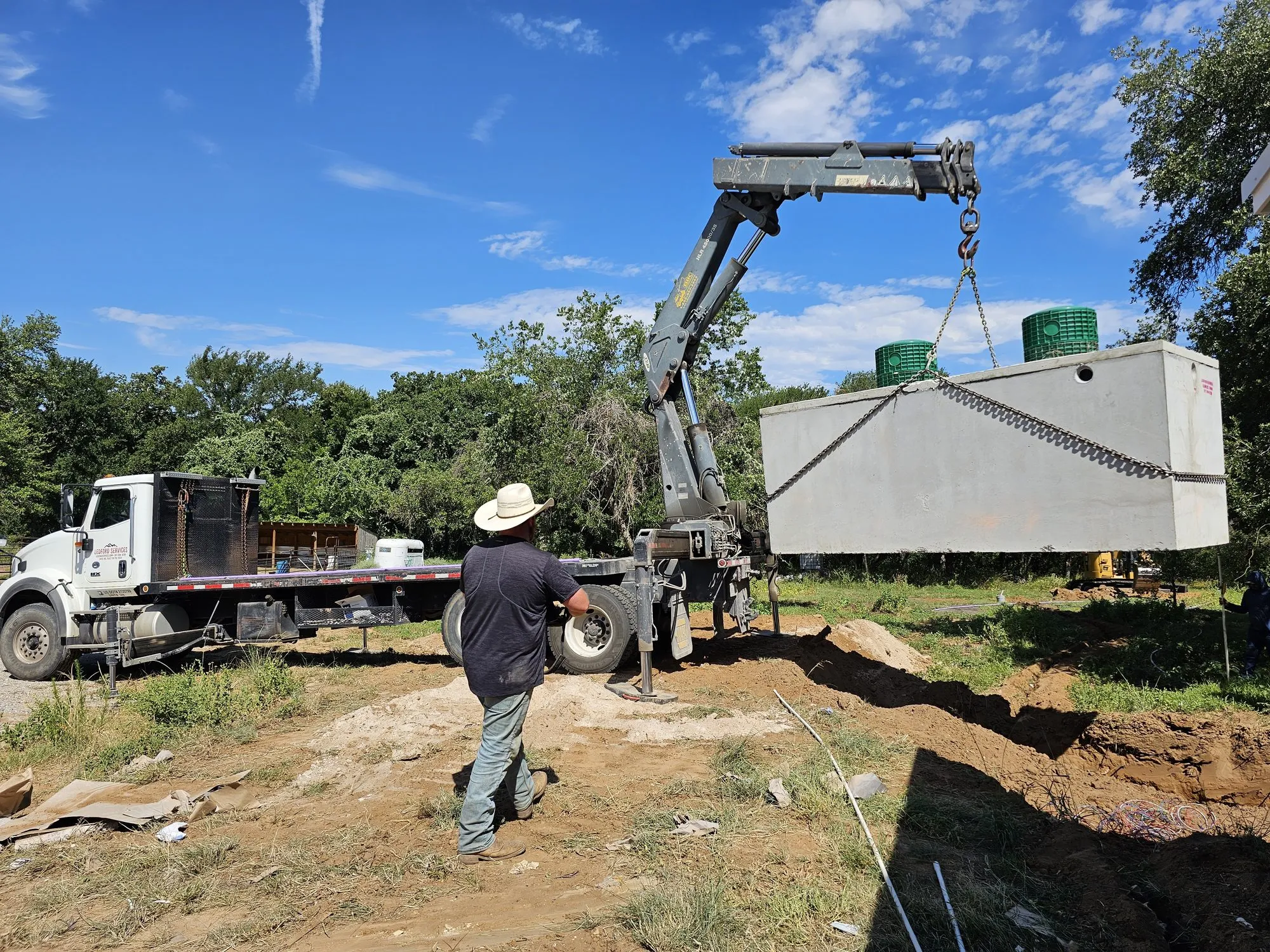 A boom truck lowering a precast septic tank into the excavation