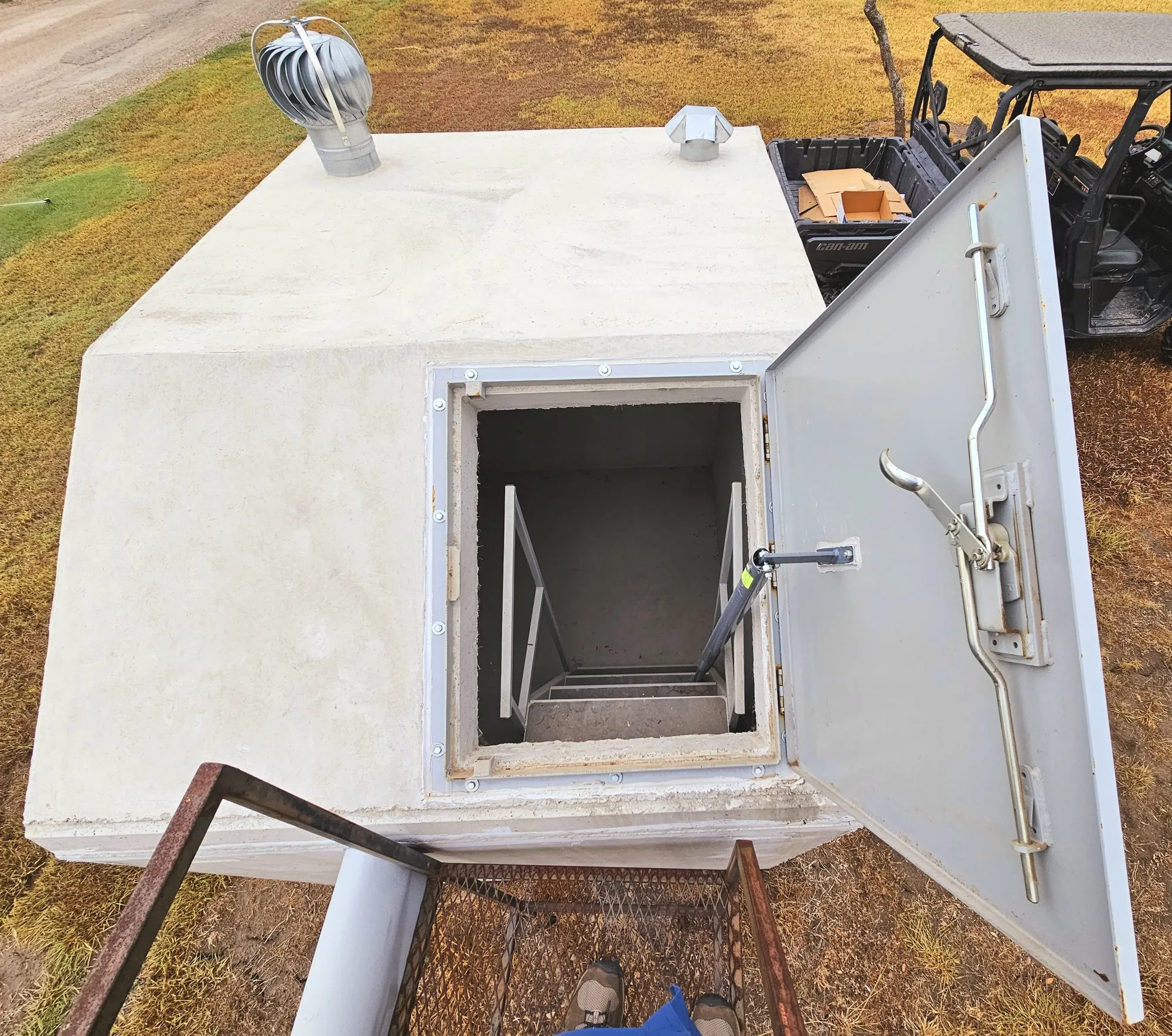 A storm shelter with its steel door swung open, showing the steps down